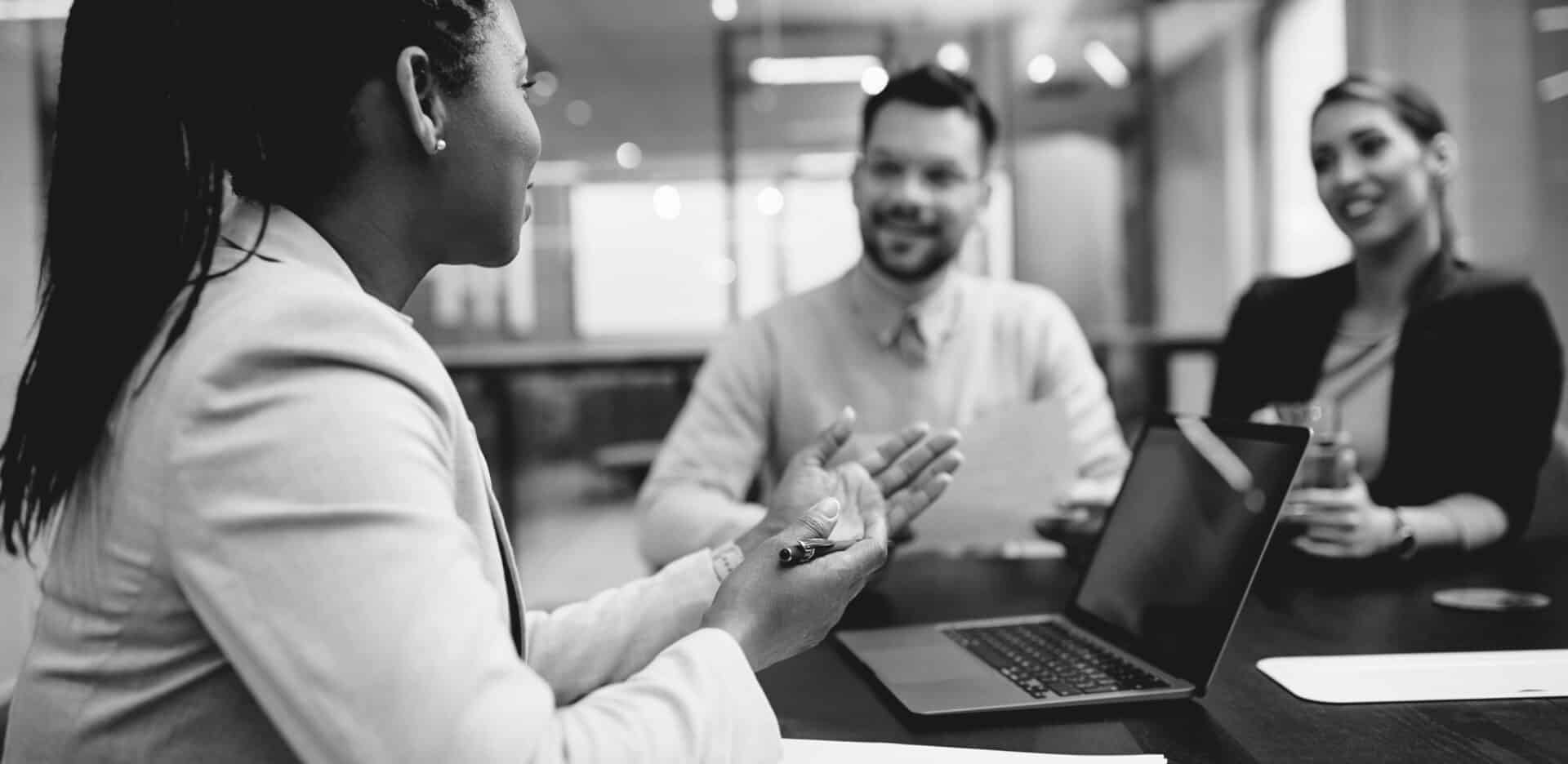 Woman in front of laptop explaining to two people, all sitting at table